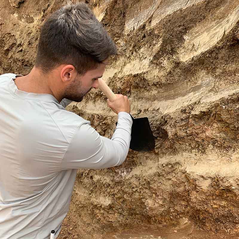 Engenheiro de minas utilizando pá para coleta de solo, dentro de uma trincheira.